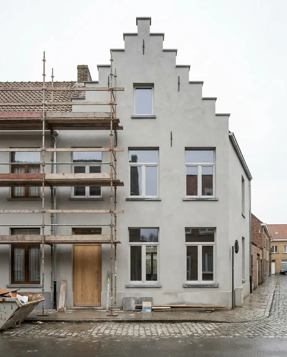 Gevel van een woning afgewerkt met lichtgrijze sierpleister, stelling nog langs één zijde