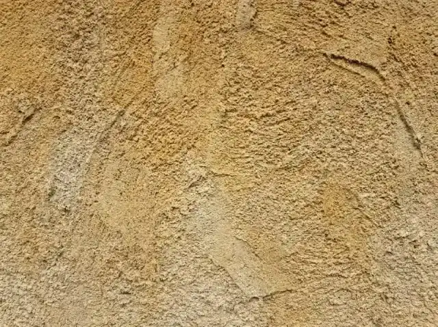 Detail van de korrelstructuur van sierpleister op een gevel, in strijklicht gefotografeerd